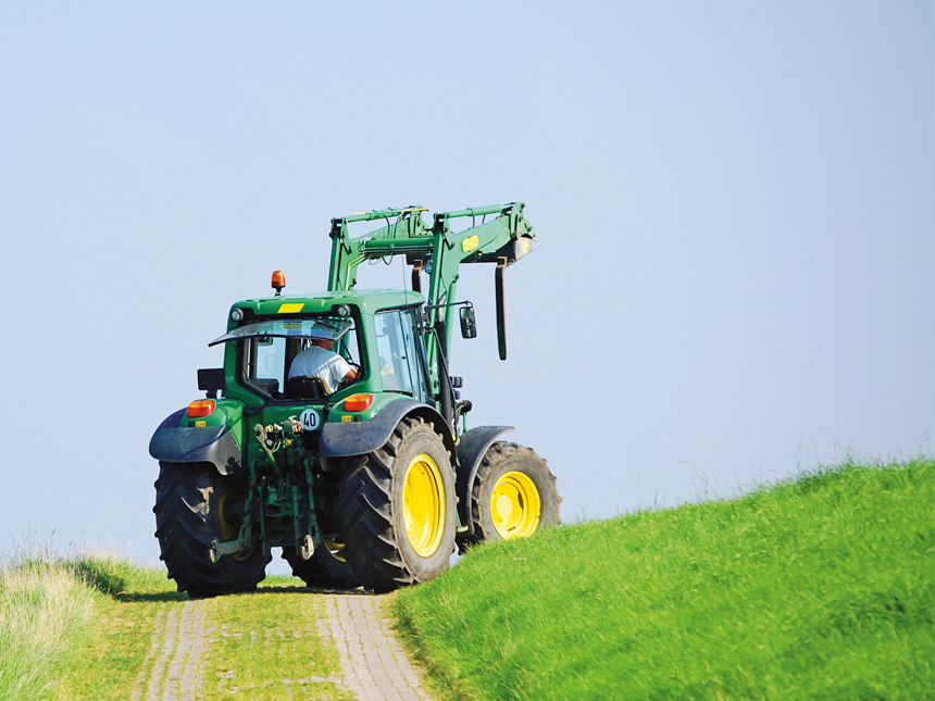 Traktor fährt mit einer Rückfahrkamera über eine Weide mit einem asphaltierten Weg