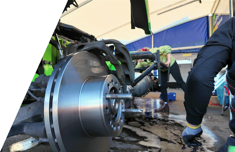 Radnabe und Bremsscheibe Nahaufnahme einer Bremsscheibe und Radnabe eines Autos, im Hintergrund arbeiten Personen in einer Werkstatt.