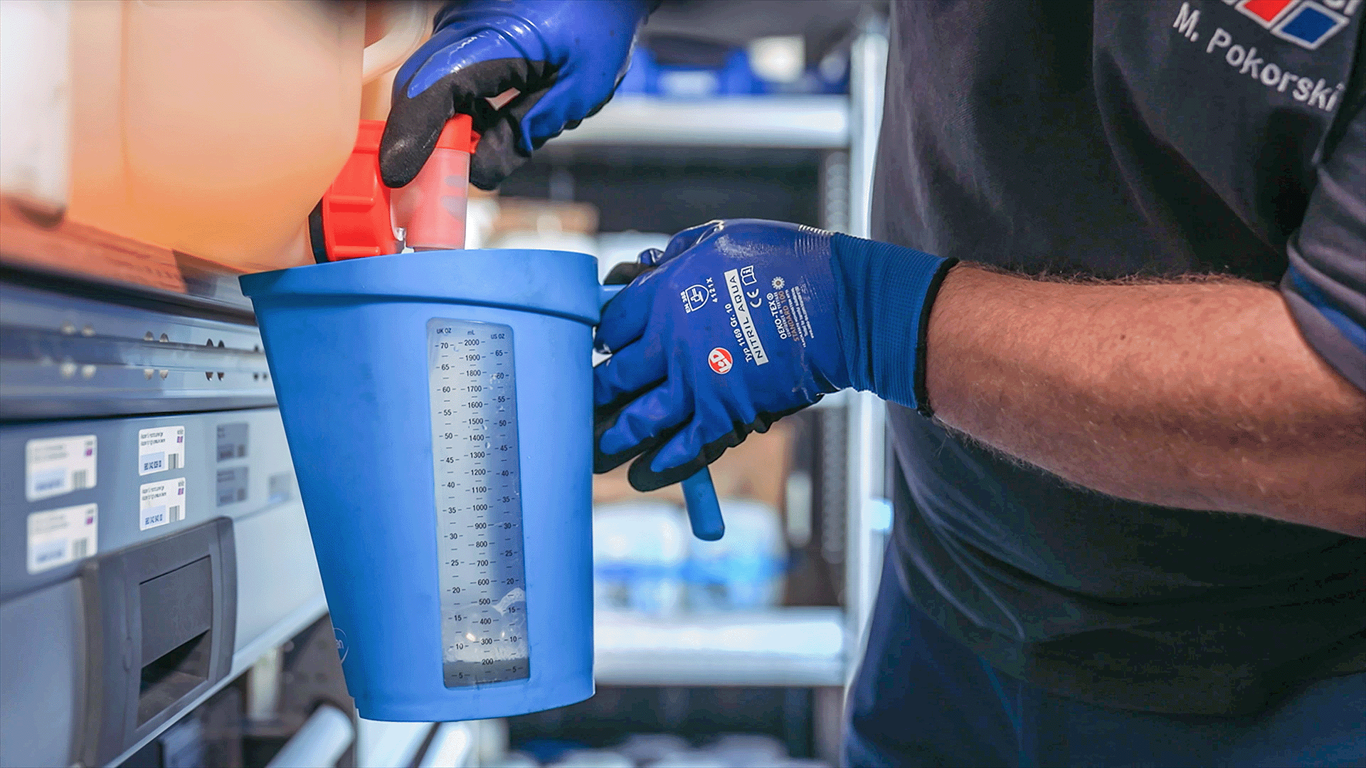 winkler Mitarbeiter mit Sicherheitshandschuhen befüllt eine Messkanne mit Reiniger